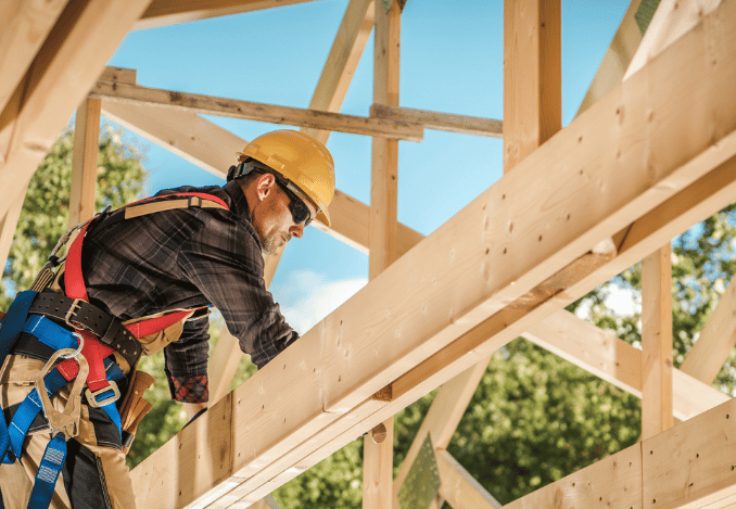 Un charpentier avec ses EPI en train de construire la charpente bois d'une maison 
